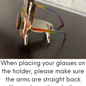 May include: A wooden glasses holder shaped like a unicorn with a rainbow mane and horn. The holder is designed to hold glasses with the arms straight back, as shown in the photo. When placing your glasses on the holder, please make sure the arms are straight back like we have them in the photo.