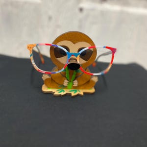 May include: A wooden sloth figurine with a colorful, patterned design, holding a pair of eyeglasses.