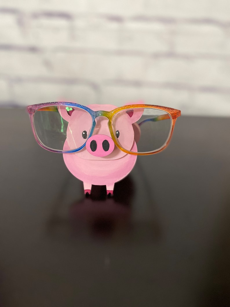 May include: A pink pig figurine wearing rainbow-colored glasses. The pig has a small snout and two black eyes.
