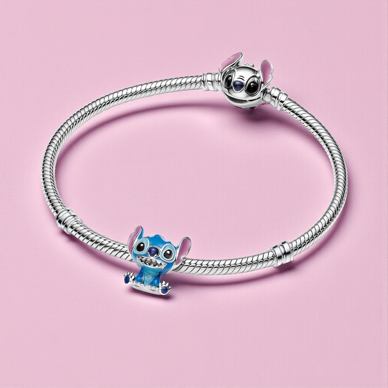 May include: A silver bracelet with two charms featuring the character Stitch from Lilo & Stitch. One charm is at the clasp, and the other is a blue Stitch charm. The background is a solid pink.