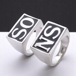 Könnte beinhalten: Zwei silberne Ringe mit schwarzem Email. Die Ringe sind rechteckig und haben die Buchstaben "SO" und "NS" in Weiß auf dem schwarzen Email.