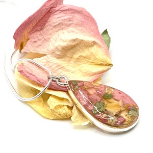 Peut inclure: Un collier en chaîne argent avec un pendentif en forme de larme rempli de pétales de fleurs roses et orange pressées et de feuilles vertes.