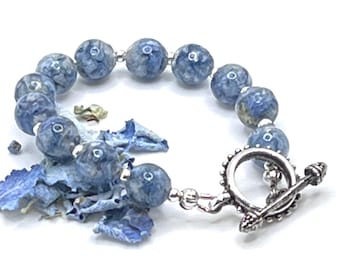 Op de afbeelding: Een blauwe en witte armband met bloemenmotief en een zilveren toggle-sluiting.
