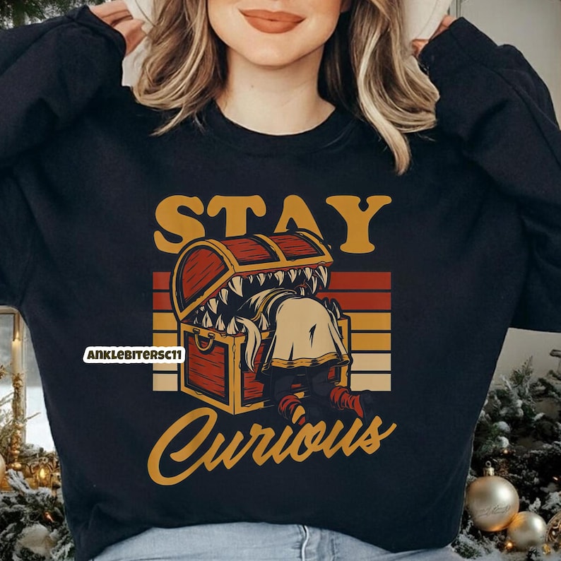 May include: Black sweatshirt with a graphic design featuring a treasure chest with a monster inside. The text "STAY Curious" is in a retro font. The design includes orange, yellow, and brown colors.