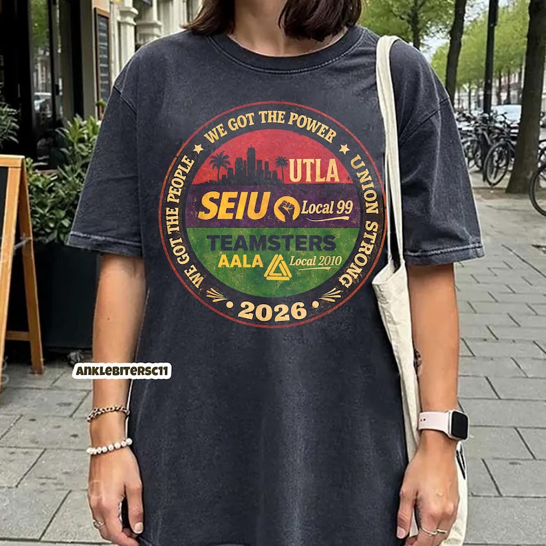 May include: Dark gray t-shirt with a circular graphic featuring the text "WE GOT THE POWER" and "UNION STRONG". The graphic includes the text "UTLA", "SEIU Local 99", "TEAMSTERS AALA Local 2010", and the year "2026".