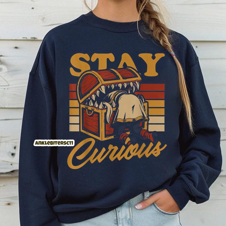 May include: Navy blue sweatshirt with a graphic design featuring a treasure chest with a monster inside. The text "STAY Curious" is above and below the chest in a vintage style.