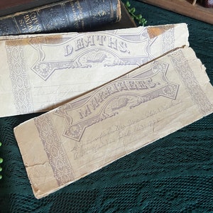May include: Two vintage, cream-colored paper forms with ornate borders and the words "Deaths" and "Marriages" printed in purple. The forms are slightly worn and have handwritten entries.