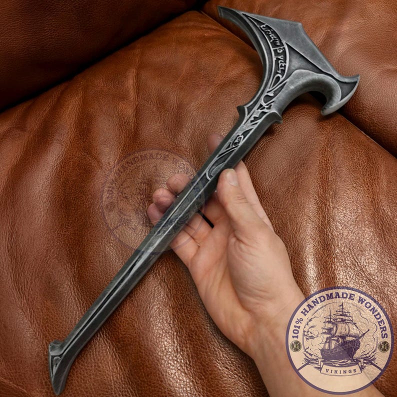 May include: A dark gray walking cane with an ornate design. The handle has a curved shape with engraved text and decorative flourishes. The shaft is long and slender, with a pointed end. The cane is held against a brown leather surface.