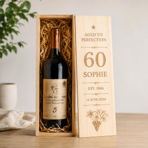 May include: A dark glass wine bottle with a cream label featuring a portrait and the number 5, nestled in a light wood box filled with straw. The box lid is engraved with AGED TO PERFECTION, 60, SOPHIE, EST. 1966, 14 JUNE 2026, and a grape vine.