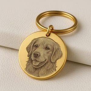 Può includere: Un portachiavi rotondo color oro con un'incisione dettagliata del volto di un cane Golden Retriever. Il pelo del cane è raffigurato con linee sottili e il ciondolo include un anello color oro per attaccare le chiavi.