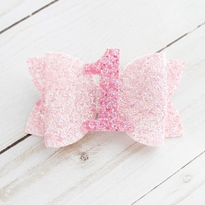 May include: Pink glitter bow with a pink glitter number one in the centre.