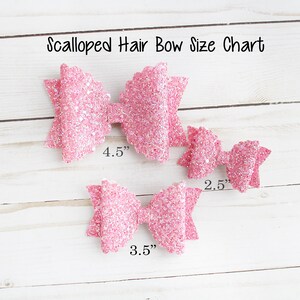 Op de afbeelding: Maattabel voor geschulpte haarstrikken. De tabel toont drie roze glitterstrikken in verschillende maten: 11,4 cm, 8,9 cm en 6,4 cm. De strikken zijn gerangschikt op een wit houten oppervlak.