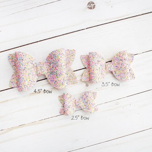 May include: Three pink glitter hair bows of different sizes. The bows measure 4.5 inches, 3.5 inches, and 2.5 inches.