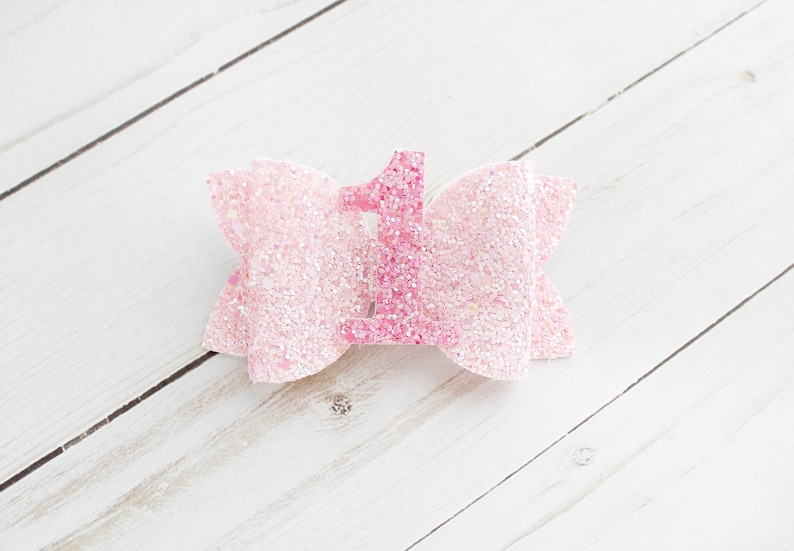 May include: Pink glitter bow with a pink glitter number one in the centre.