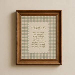 Op de afbeelding: Een ingelijste print met een houten frame. De print heeft een lichtgroene en witte ruitpatroonrand. Het midden heeft de tekst "THE BLESSING" en een gebed. Het frame is donkerbruin.