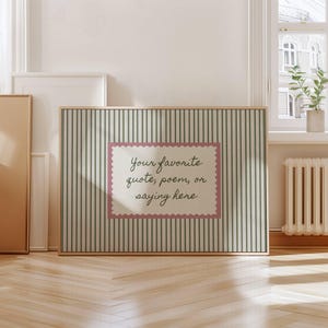 May include: A rectangular framed print featuring a light green and white vertical striped background. In the center, a cream-colored rectangular label with a scalloped pink border displays the black cursive text: Your favorite quote, poem, or saying here.