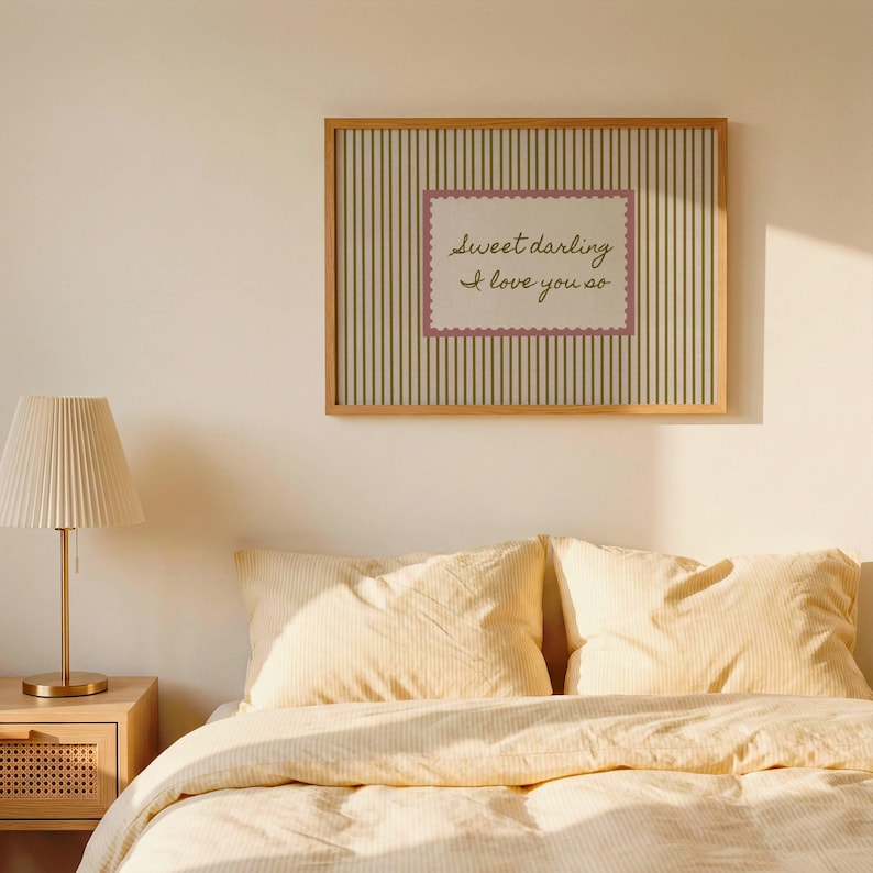 May include: A rectangular wall art print in a light wood frame featuring a vertical olive green and cream striped background. Centered is a cream-colored rectangular label with a scalloped pink border containing the text Sweet darling I love you so.