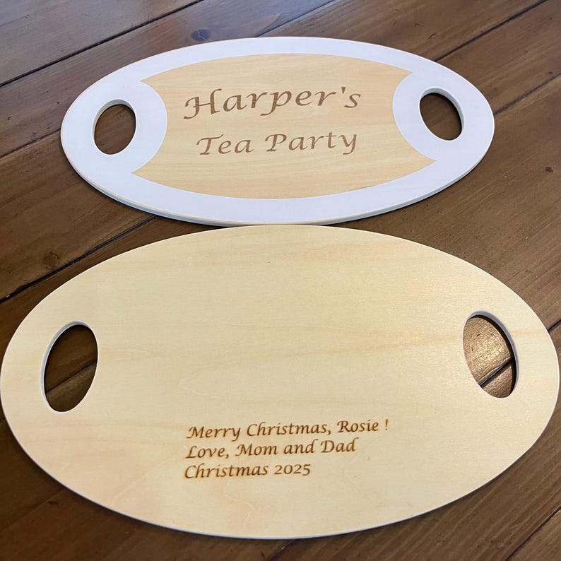 May include: Two wooden serving trays. One tray has the text "Harper's Tea Party" in a light brown font. The other tray has the text "Merry Christmas, Rosie! Love, Mom and Dad Christmas 2025". Both trays have oval shapes with handle cutouts.