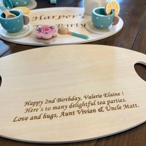 May include: Wooden tea party set with a serving tray and a smaller tray with tea cups, spoons, and a flower-shaped cookie. The serving tray has handles and engraved text: "Happy 2nd Birthday, Valerie Elaine!"
