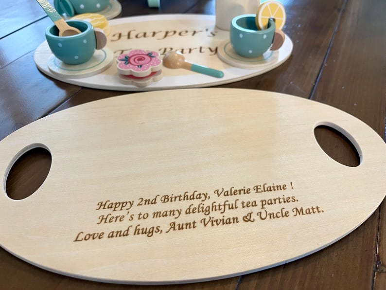 May include: Wooden tea party set with a serving tray and a smaller tray with tea cups, spoons, and a flower-shaped cookie. The serving tray has handles and engraved text: "Happy 2nd Birthday, Valerie Elaine!"