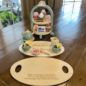 May include: A wooden tea set with a three-tiered serving tray, teapot, cups, and treats. The set includes a serving tray with the text "Harper's Tea Party". A wooden serving tray with handles is also included.