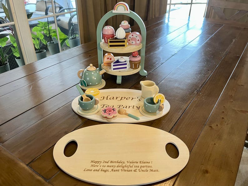 May include: A wooden tea set with a three-tiered serving tray, teapot, cups, and treats. The set includes a serving tray with the text "Harper's Tea Party". A wooden serving tray with handles is also included.