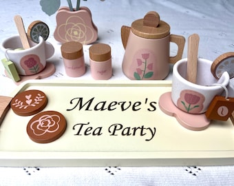 May include: A wooden tea set with a pink teapot, two cups, two small containers, and a tray with the words "Maeve's Tea Party".