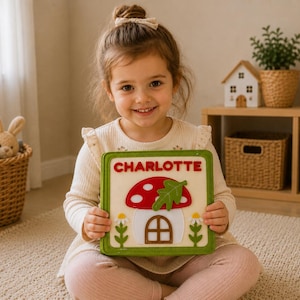 May include: A square wooden puzzle board featuring a red and white mushroom house design with a green leaf accent. The name CHARLOTTE is printed in red capital letters at the top. The board has a green border and includes white daisy flowers.