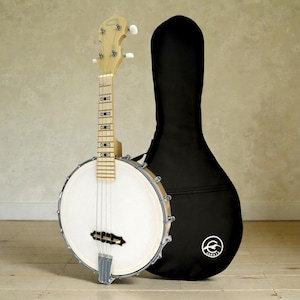 May include: A banjo with a white drumhead and a light-colored wooden neck and headstock. The banjo has four strings and metal hardware. A black banjo case is behind the instrument.