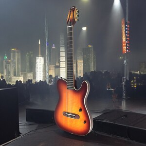 May include: A brown and black acoustic guitar with a sunburst finish on a stage in front of a city skyline at night.