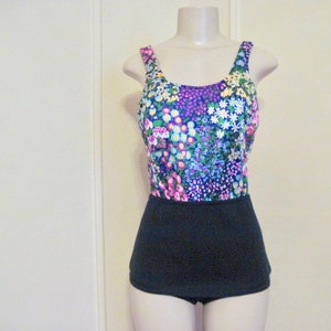 May include: A vintage floral print swimsuit with a black skirt. The swimsuit has a scoop neck and thin straps. The floral print is in shades of pink, purple, blue, green, and yellow.