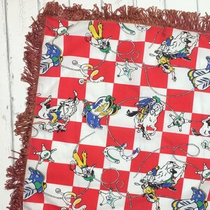 May include: A red and white checkered throw pillow with a fringe border. The pillow features a repeating pattern of cowboys riding horses, stars, and horseshoes.