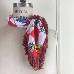 May include: A red and white checkered scarf with a fringe border. The scarf features a colorful cartoon design of people riding horses. The scarf is tied around a white mannequin's neck. The mannequin has the words "ROYAL FORM" printed on the top of its head.