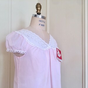 May include: A pink cotton nightgown with white eyelet lace trim around the neckline and sleeves. The nightgown has a v-neck and short sleeves. The nightgown has a tag that says "Canadian Made".