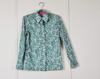 Puede incluir: Una camisa de manga larga con un cuello grande, con estampado floral verde y blanco.