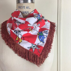 May include: A red and white bandana with a checkered pattern and a fringe border. The bandana features a colorful illustration of cowboys roping a calf.