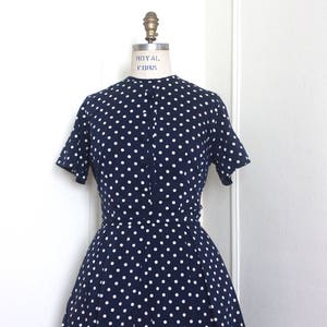 May include: A navy blue dress with white polka dots. The dress has short sleeves and a button-up front.