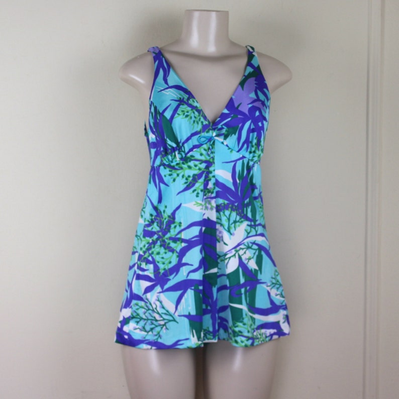 May include: A blue and green floral print swimsuit with a V-neck and a button closure. The swimsuit has a short skirt and thin straps.