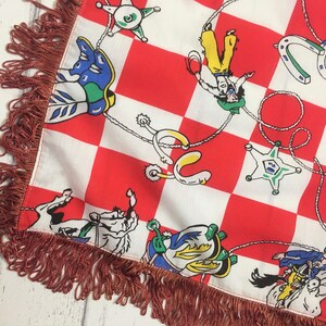 May include: Red and white checkered fabric with a fringe border. The fabric features a repeating pattern of cowboys, horses, and horseshoes.