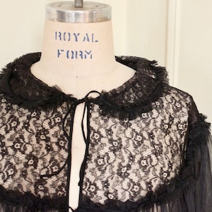 May include: A black lace robe with a ruffled collar and tie closure. The robe is made of sheer fabric and has a delicate floral pattern.
