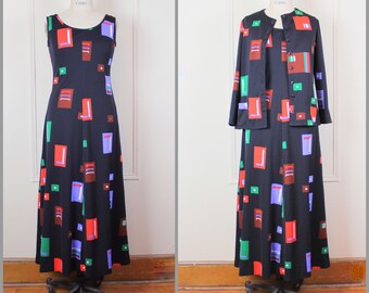 May include: A black maxi dress with a geometric pattern in red, green, blue, and brown. The dress has a sleeveless design and a fitted bodice. The dress is paired with a matching black jacket with long sleeves and a geometric pattern.