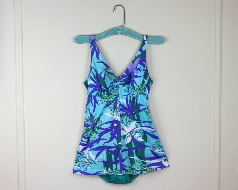 May include: A blue and green swimsuit with a floral print. The swimsuit has a V-neck and a skirt.