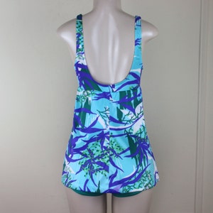 May include: A blue, green, and purple swimsuit with a floral print. The swimsuit has a scoop neck and a wide, adjustable strap.