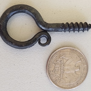 May include: A dark metal eye screw with a spiral threaded shank. The eye is circular with a small curled end. A U.S. quarter is next to the screw for size comparison.