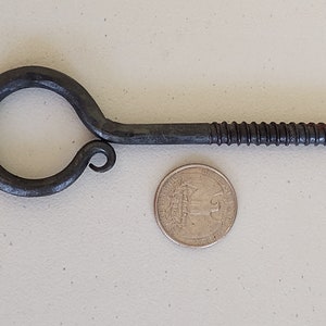 May include: A black metal hook with a screw thread and a loop at the end. The hook is about the size of a US quarter.