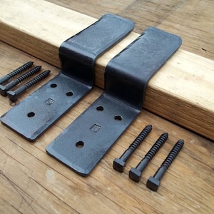 May include: Two black metal shelf brackets with a curved design, each with three pre-drilled holes and a decorative stamp. Includes black screws for installation. The brackets are shown on a wooden surface.