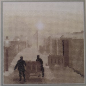 May include: A cross-stitch artwork depicting two figures walking down a foggy street in a town. The figures are silhouetted against the white fog, and the buildings on either side of the street are barely visible.