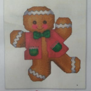 May include: A gingerbread boy wearing a red jacket with green trim and a green bow tie. The gingerbread boy is smiling and has white icing on his head and arms.