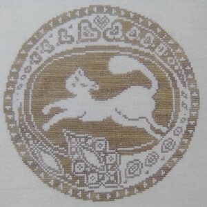 May include: A white cat silhouette embroidered on a beige fabric background. The cat is running and jumping in a circle with a decorative border.