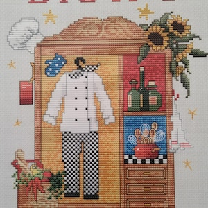 May include: Cross-stitch embroidery design featuring a wooden cabinet with a chef's uniform inside. The cabinet has shelves with bottles, a red pot with whisks, and drawers. The cabinet is decorated with sunflowers and stars. The text "Bistro" is above the cabinet.